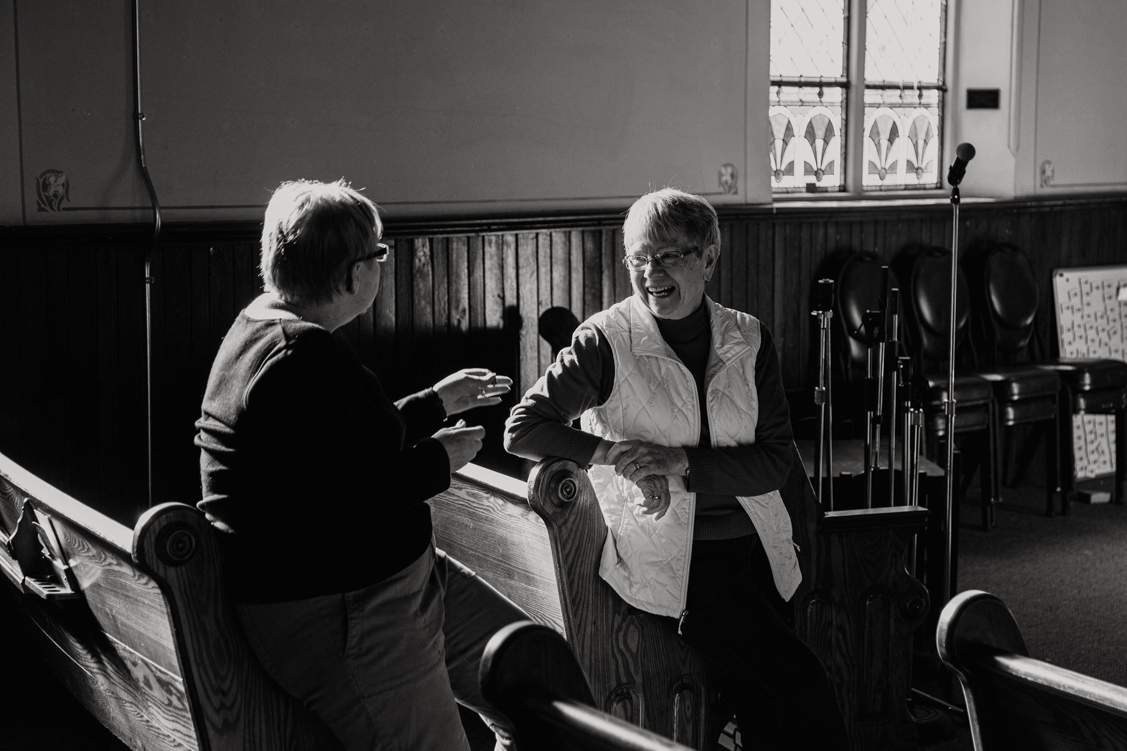Two people standing in a church pew, engaged in conversation.